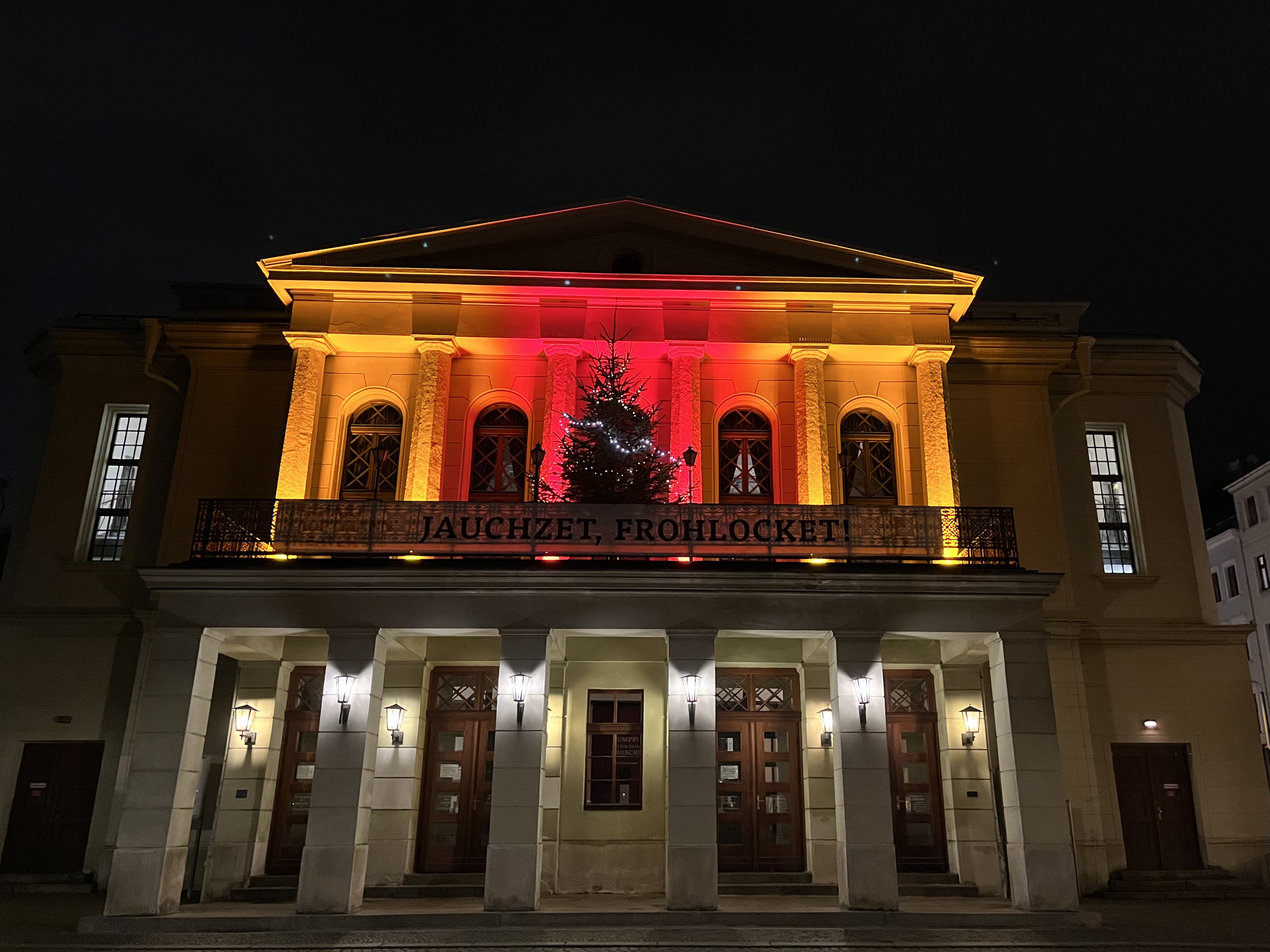 Blick auf die in rot und orange ausgeleuchtete Vorderseite des Theater in Görlitz