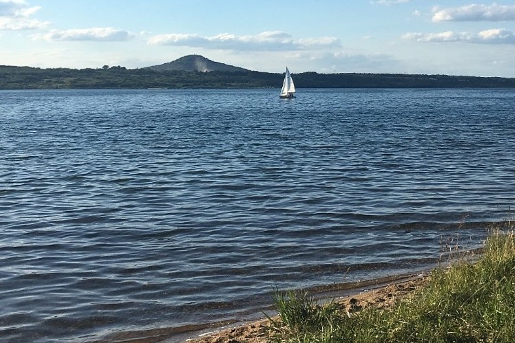 Blick auf den Berzdorfer See. Im Hintergrund ist ein Segelboot.